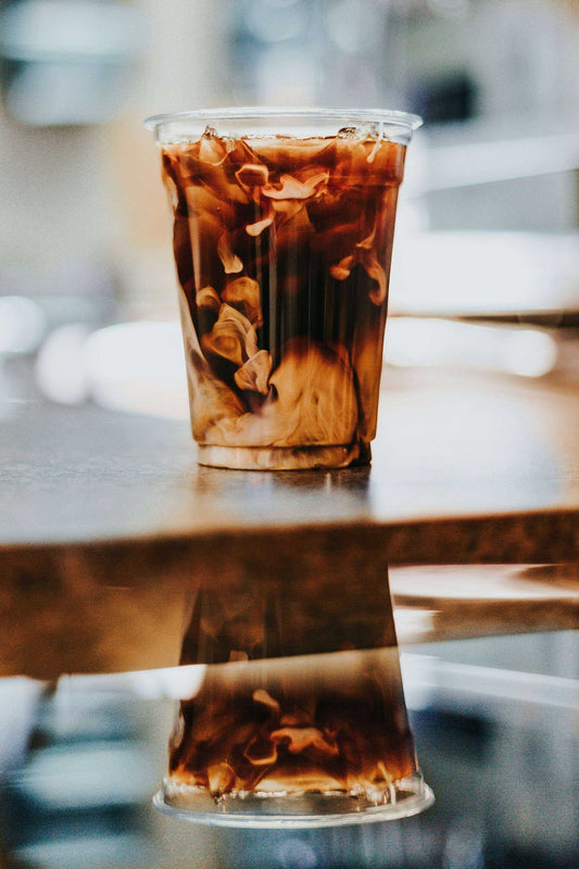 Kalter Cold Brew Kaffee im Plastikbecher mit Milchwirbeln auf Holztisch